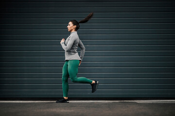 An urban sportswoman in shape is running on the city street downtown.