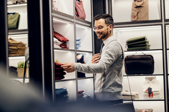 A happy young man in smart causal is standing in store and choosing shirts.