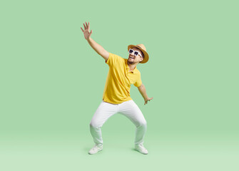 Funny man in casual summer clothes dancing on light green studio background. Happy young traveler...