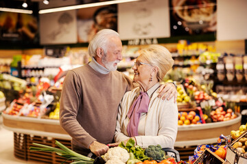 A happy senior couple is hugging at the supermarket while shopping.