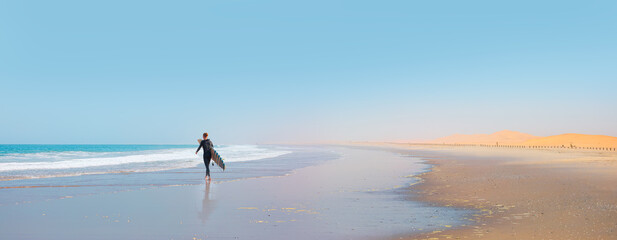 A male surfer walks on the beach with a surfboard in hand - Skeleton coast, Namibia