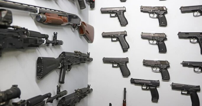 Gun shop or handing out pistols, rifles, revolvers in a shooting range. Storehouse of different types of weapons hanging on the wall. Sliding shot indoors, close-up
