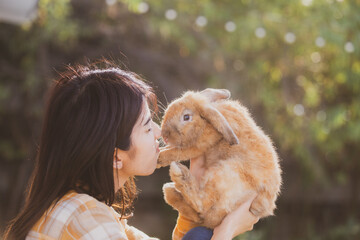 Young smiling and innocent girl holding and hugging a cute little rabbit with closed eyes and...