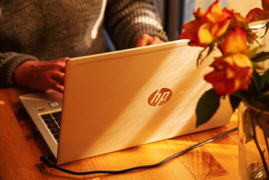 Paris, France - February 9, 2022: Man working from home at simple workplace with HP laptop computer in sunset light. Remote working from home in comfortable working environment.