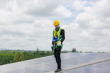 Obraz premium Handsome young male engineer wearing safety vest and jacket with gloves and tools along with hard hat helmet standing on solar panel while checking and looking at its maintenance