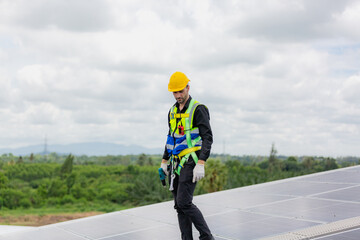 Obraz premium Handsome young male engineer wearing safety vest and jacket with gloves and tools along with hard hat helmet standing on solar panel while checking and looking at its maintenance
