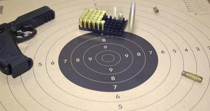 Gun and empty bullet shells on paper target shooting practice. Bullet casings fall down on the target, closeup, slow motion