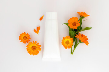 White plastic tube with face, hand and body cream and calendula,marigold flowers. Organic cosmetic concept,template . Flat lay,copy space. - obrazy, fototapety, plakaty