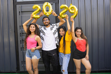Happy group of indian friends with golden 2029 balloons outdoor. New Year celebration.