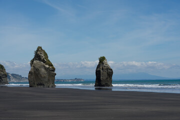 Strand mit schwarzem Sand und Felsen und Pfützen in Neuseeland bei den Three Sisters.