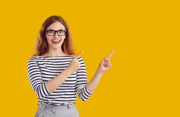 Portrait of young excited woman in glasses, striped blouse and grey pants with wavy hair pointing...