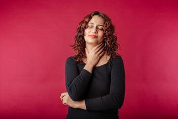 Fototapeta premium Woman standing isolated over red background holding her inflamed throat. Medical concept, Sore throat. Having sore throat, holding hand on her neck, suffering from throat pain, painful swallowing.