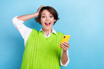 Photo of funny surprised overjoyed girl wear green knitted vest hand head open mouth betting online win lottery isolated on blue color background