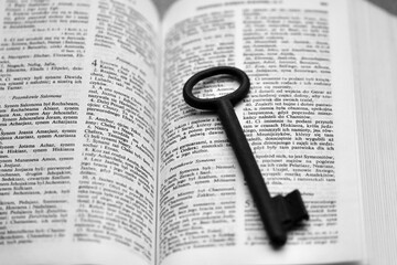 Fototapeta premium Otwarty tekst Ewangelii z kluczem na wierzchu - symbol poznania i wiary. Biblia i zachęta do czytania, studiowania Słowa Bożego