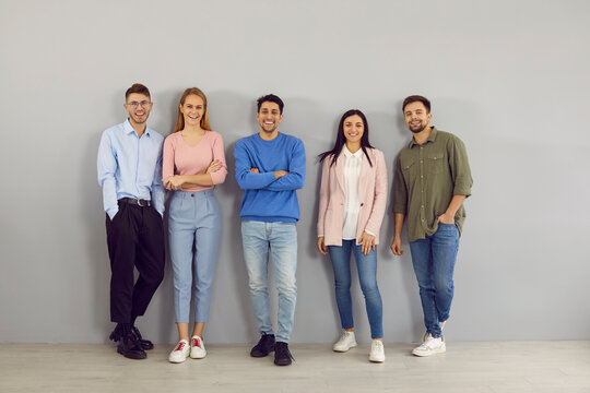 Confident toung team. Portrait of group of different positive smart young people on gray wall background. Men and women in stylish smart and casual clothes stand in row and smile looking at camera.