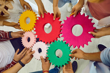Team of people, students or corporate workers, standing in circle, holding colorful cogs and joining them. Cropped shot of hands with gears. Teamwork, business, education, success concept background