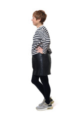 side view full length portrait of a woman in skirt, striped sweater and sneakers with arms akimbo on white background