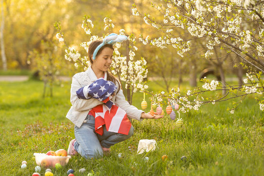 A teenage girl in a blooming garden at Easter with a US flag