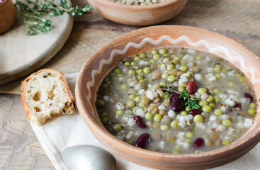 Bean soup in a ceramic bowl with a sprig of thyme and a piece of bread on a wooden table. A mix of red beans, lentils and peas. The concept of vegetarian food. Rustic style. Horizontal orientation.