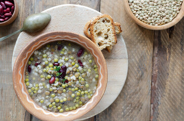 Bean soup in a ceramic bowl with a sprig of thyme on a wooden table. A mix of red beans, lentils and peas. The concept of vegetarian food. Rustic style. Horizontal orientation. Top view