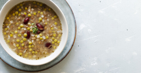 Bean soup in a ceramic gray bowl with a sprig of thyme and a piece of bread on a grey background. A mix of red beans, lentils and peas. The concept of vegetarian food. Top view. Copy space Banner
