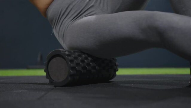 Muscle recovery after a hard workout. Close-up of a young athletic woman using a foam roller to roll out back muscles and legs