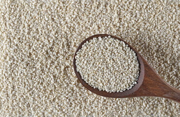 White hulled sesame seeds in wooden spoon background and texture 