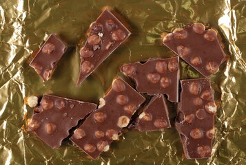 Chocolate bars set with hazelnut, pieces on golden aluminum foil, top view
