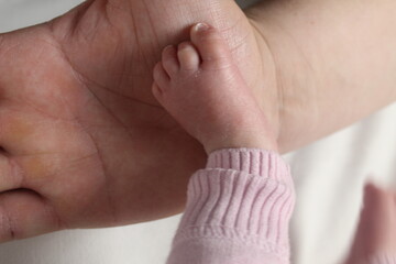 a small leg of a baby born on the arm of a man's father in close-up. Father and child daughter