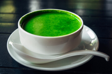 Green spinach soup in a white round plate with a spoon on a dark background. Vegetarian food
