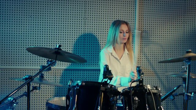 Blonde girl is learning to play drums, cymbals. Female drummer is rehearsing before concert. Young woman tympanist performs musical composition on percussion instruments in recording studio