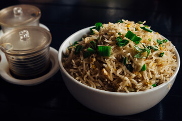 Fried rice with chicken and green onions on a white plate on a dark background with a set of spices. Delicious dish on a dark background with a copy space