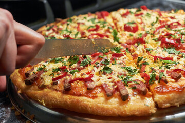 Cutting pizza into pieces in close-up. Vegetable pizza with cheese