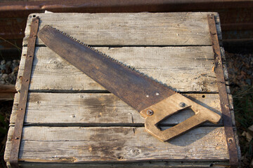 An old hacksaw is lying on a wooden box