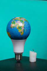 Light bulb with Earth planet model with space for text. Nearby is a candle stub. Global ecology, International Day of Energy Saving or Earth Hour concept. On a turquoise background.