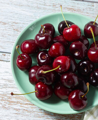 Top view of ripe cherries on a green plate on a wooden background.