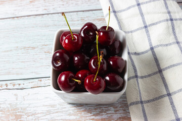 Top view of sweet ripe cherries in a ceramic bowl on a wooden background.