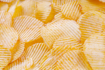 Yellow crispy ridged potato chips close up. Food background, banner, header, wallpaper.