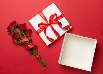 Open gift box with red roses on color background, top view