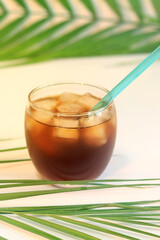 Iced coffee. Glass with a drink with ice and palm leaves. Cold summer drink and drinking straw. Refreshing cocktail