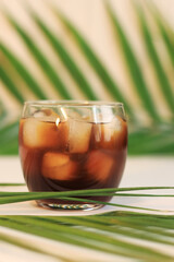 Iced coffee. Glass with a drink with ice and palm leaves. Cold summer drink