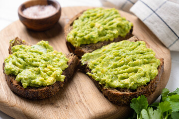Vegan avocado and rye bread toast on wooden board, closeup view