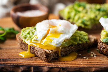Delicious breakfast rye bread toast with mashed avocado and poached egg, closeup view