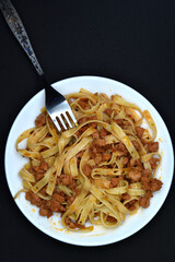 Italian pasta on a white plate with a fork. A plate of vermicelli with meat on a black background.