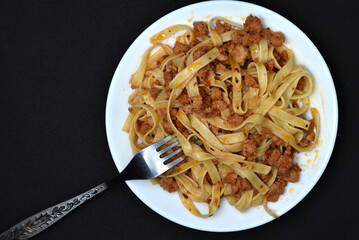 Italian pasta on a white plate with a fork. A plate of vermicelli with meat on a black background.