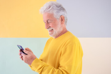 Smiling bearded senior man in yellow using mobile phone . Handsome old grandfather standing on a colorful isolated background enjoying tech and social