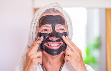 Smiling senior beautiful woman applying a detox facial charcoal mask homemade - wellness, take care...