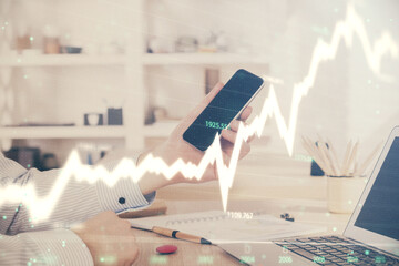 Double exposure of man's hands holding and using a digital device and forex graph drawing. Financial market concept.