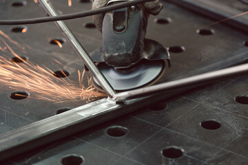 Worker in metal factory grinding workpiece with disk grinder, sparks flying