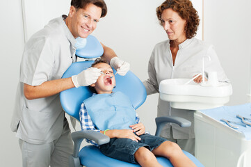 Obraz premium dentist examining teeth of boy. dentist in gloves using tooth on teeth of little patient while cute boy looking at camera during checkup procedure. Assistant in background